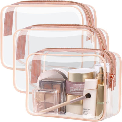 Set of three PVC transparent makeup bags with rose gold zippers, various sizes, holding cosmetic products and brush.
