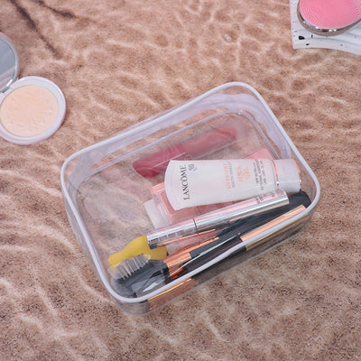 Clear PVC transparent makeup bag with cosmetics and brushes inside on a soft textured surface